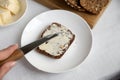 healthy whole-grain bread without flour a slice lies on a white plate a womanÃ¢â¬â¢s hand spreads butter with a knife Royalty Free Stock Photo